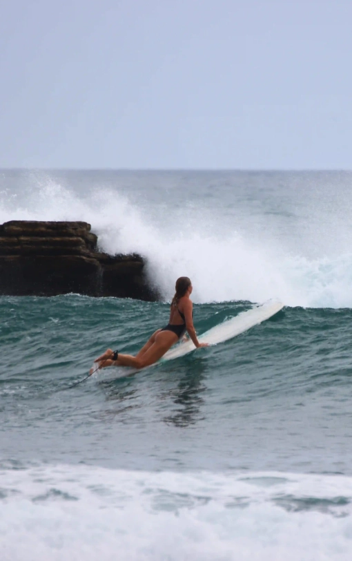 Surfer paddling into a breaking wave near Magnific Rock in Popoyo, Nicaragua, with rocky reef formations