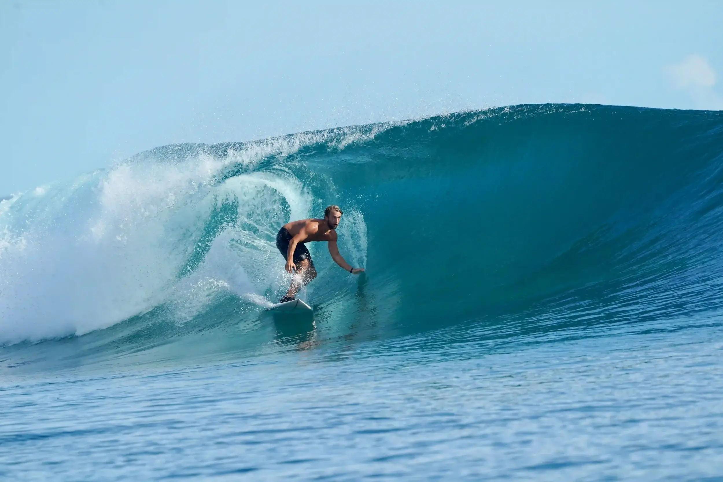 A surfer riding inside a clear turquoise barrel on a calm, sunny day.