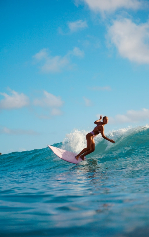 A surfer performing a smooth turn on a small clean wave under a bright blue sky.