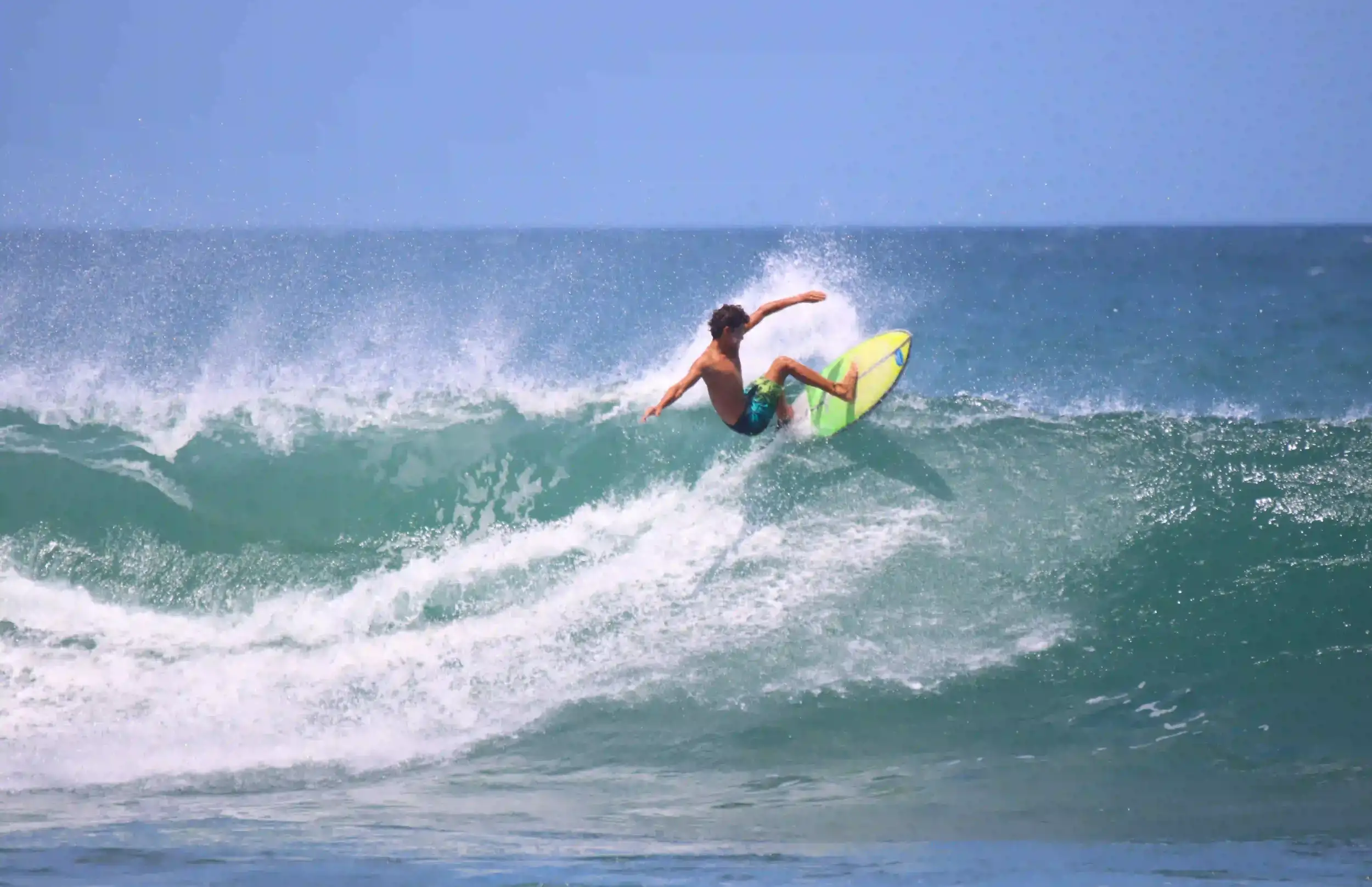 An advanced surfer performing a sharp turn on a green wave under clear skies.