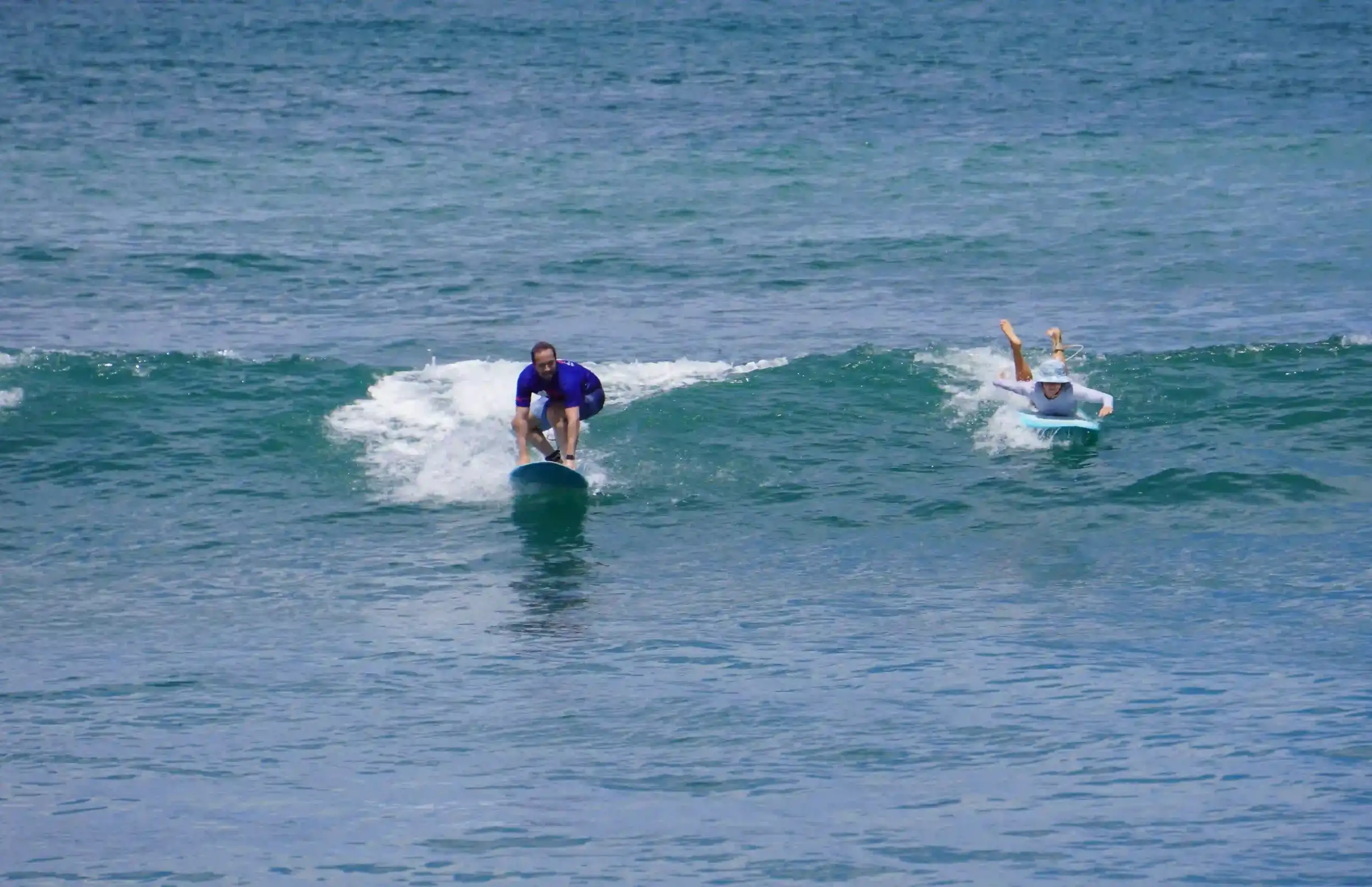 A beginner surfer catching a small wave while another paddles nearby.