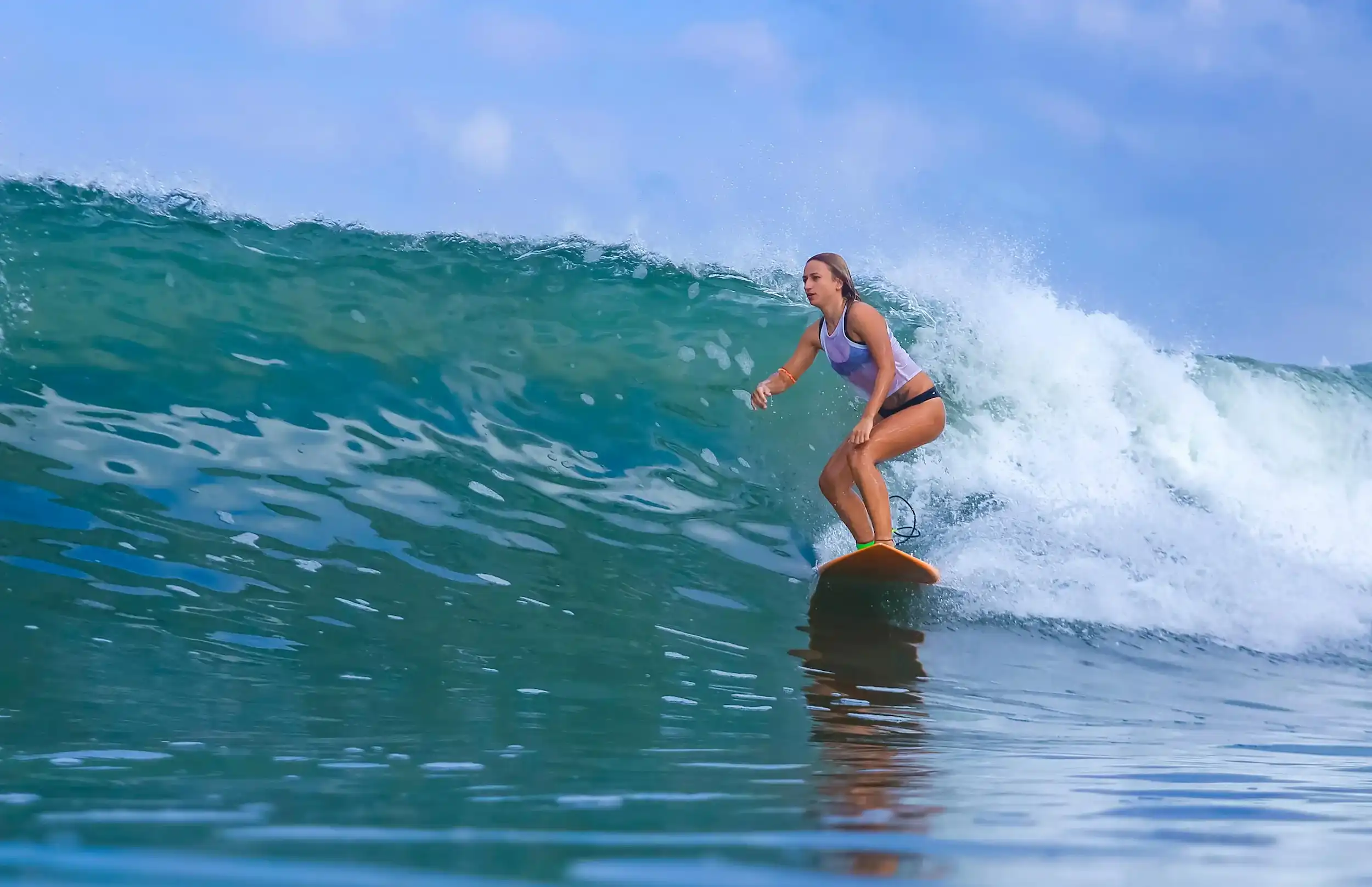 An intermediate surfer riding a clean green wave under clear skies.