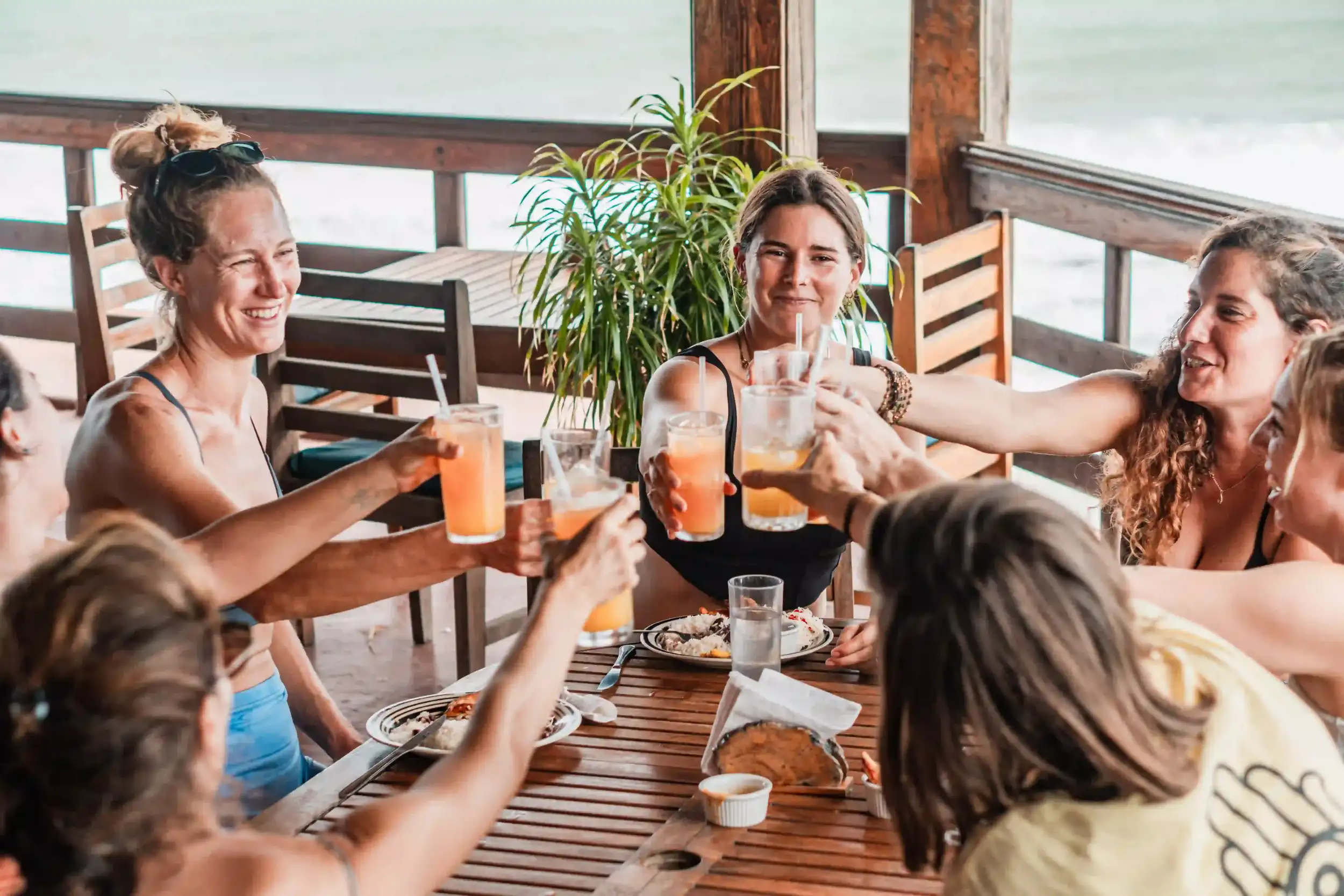 A group of guests enjoying drinks and food together at an oceanfront restaurant.