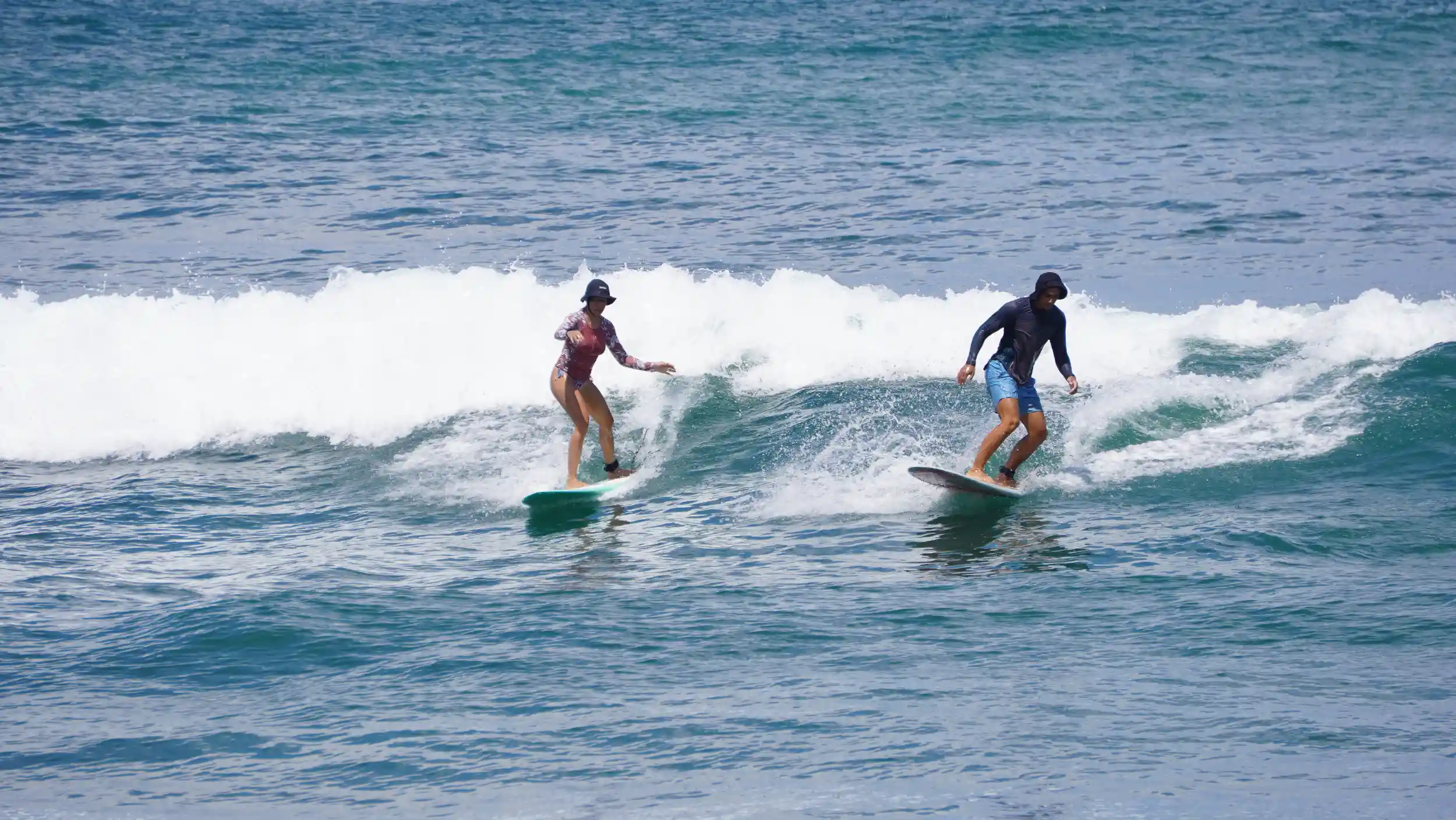 Two beginner surfers riding the same small, clean wave at Beginners Bay Popoyo, enjoying calm surf conditions ideal for learning.