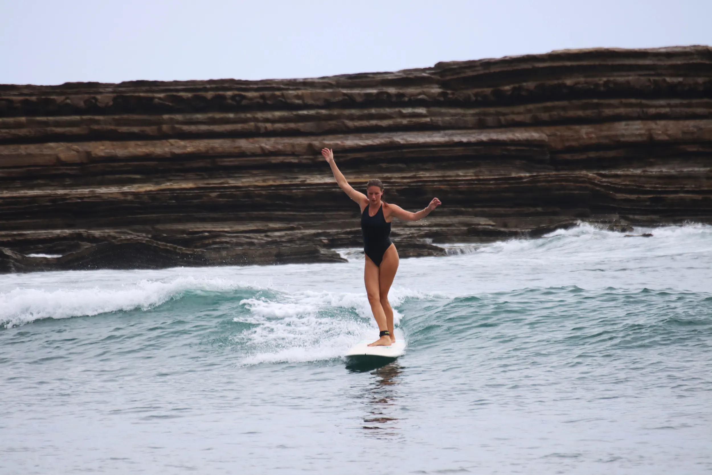 Beginner surfer riding a small, clean wave at Beginners Bay Popoyo with rocky reef backdrop and calm surf conditions ideal for learning.