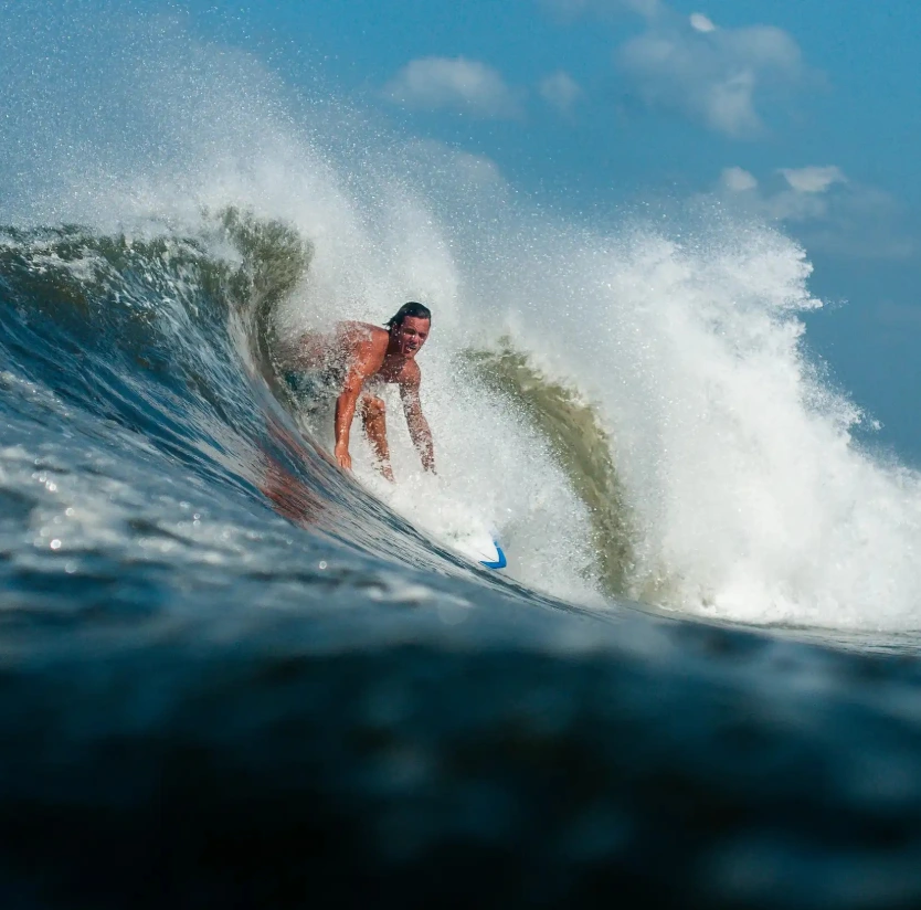 Surfer riding inside a clean, powerful wave in Nicaragua, surrounded by whitewater spray and clear blue sky