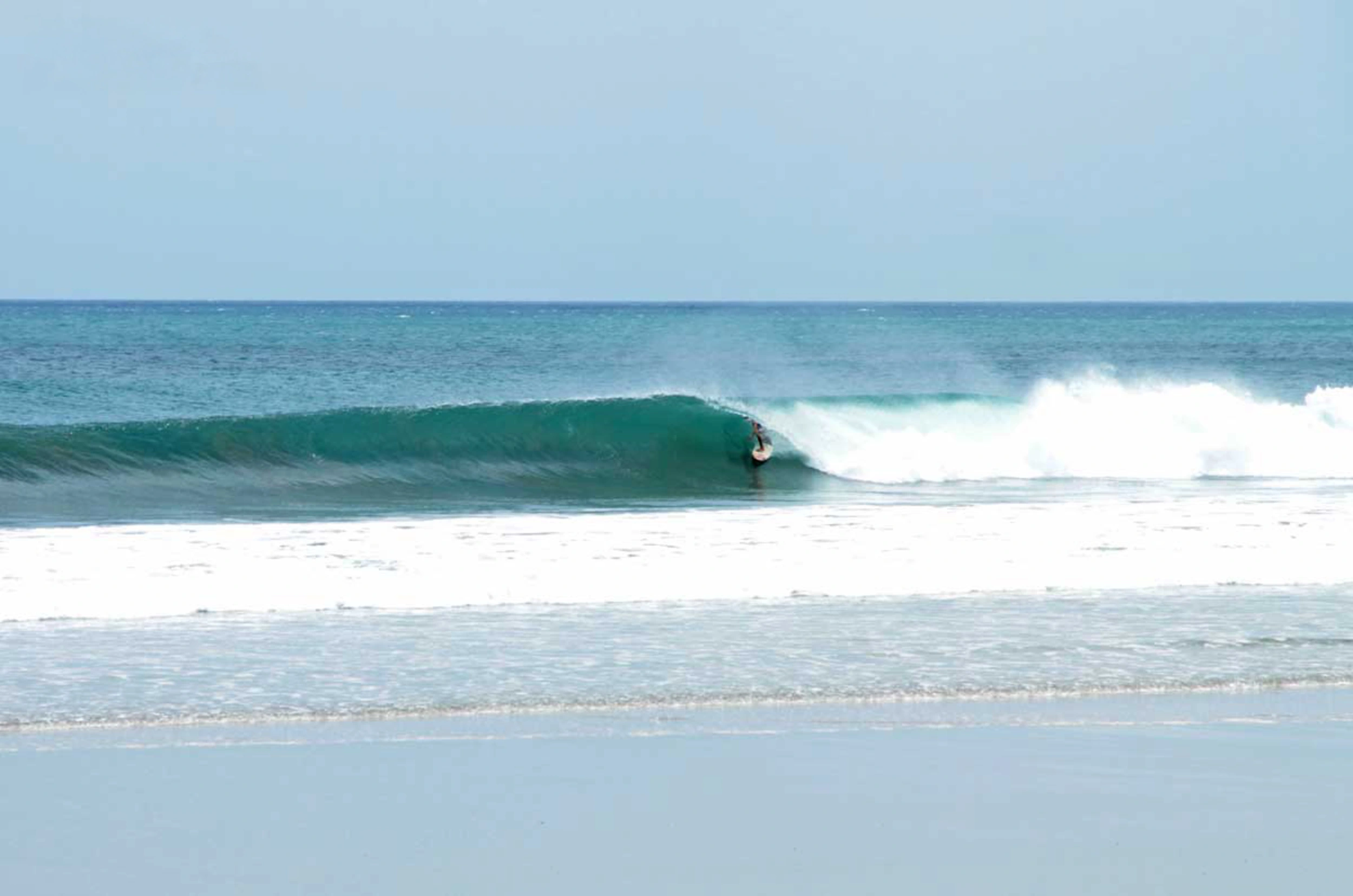Surfer tucked into a clean, hollow wave at Playa Colorado, with smooth offshore winds and classic fast beach-break conditions.