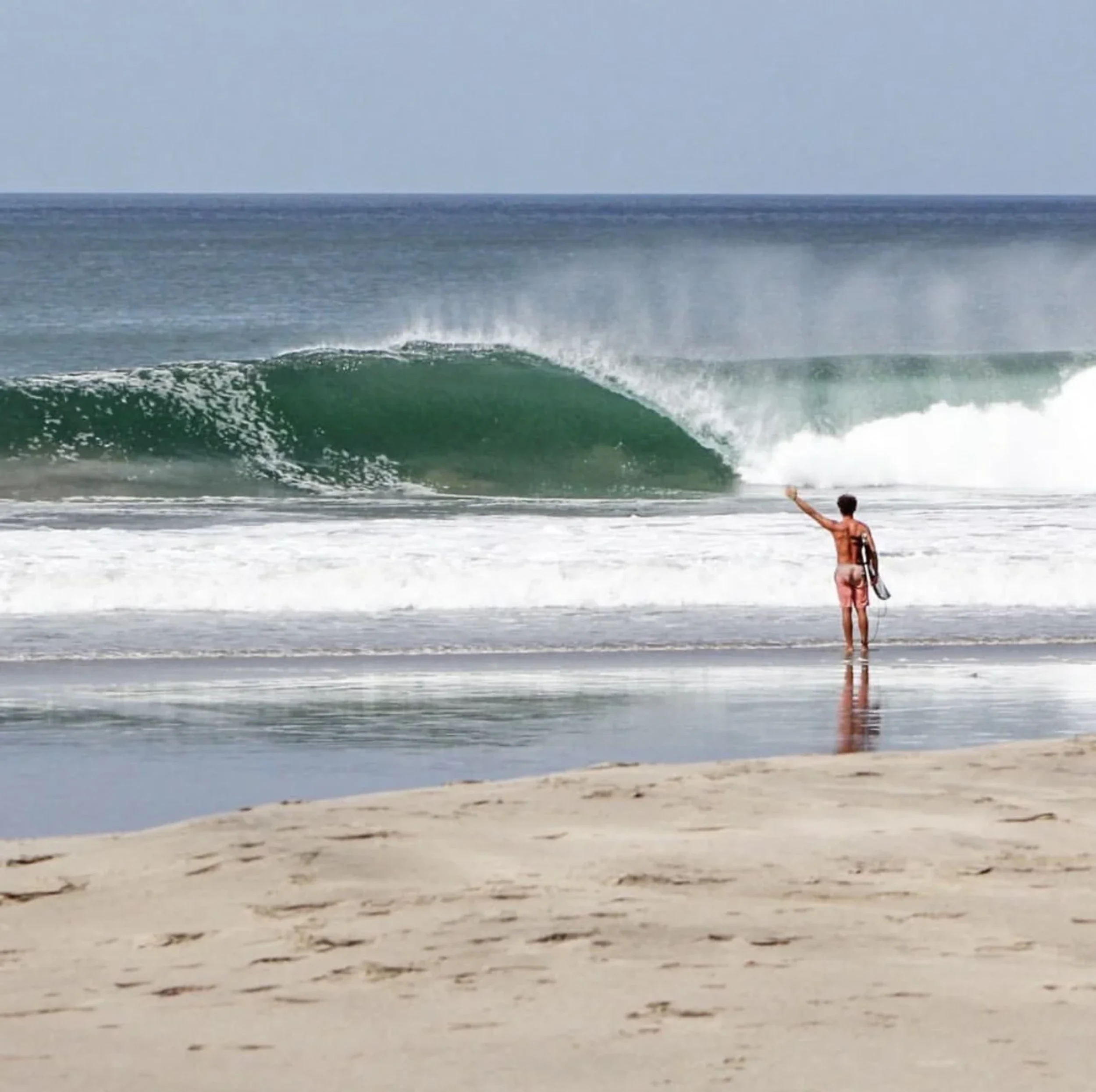 Surfer standing on the beach at Playa Colorado watching a perfect hollow peak break with clean offshore winds and glassy conditions.