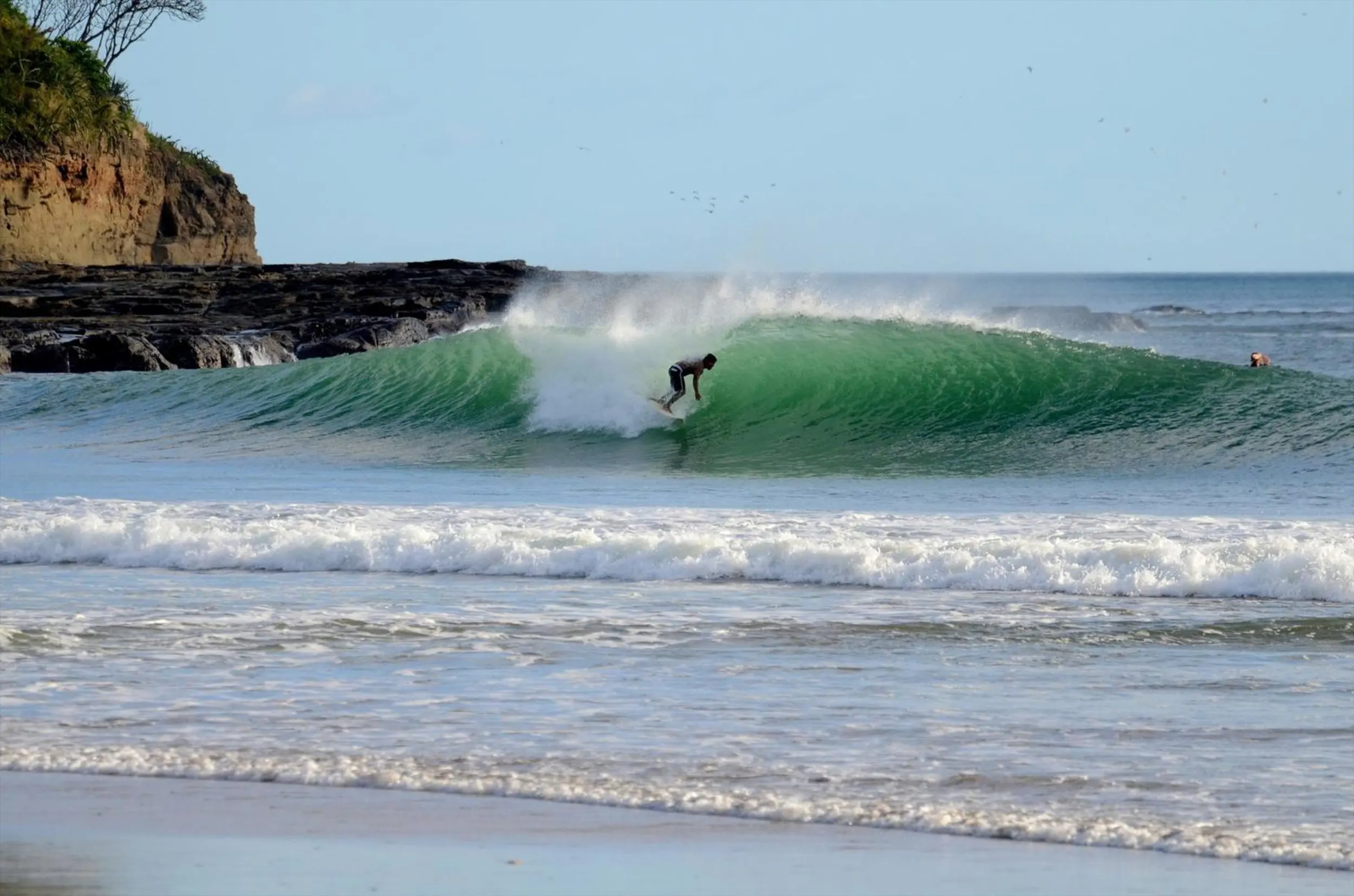 Surfer riding a clean, green barrel at Playa Santana with rocky reef backdrop and smooth, powerful wave conditions