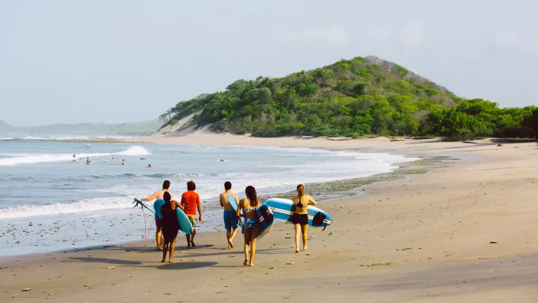 Group of surfers walking along the beach at Popoyo Reef carrying surfboards toward the waves, with tropical coastline and open sandy shoreline.