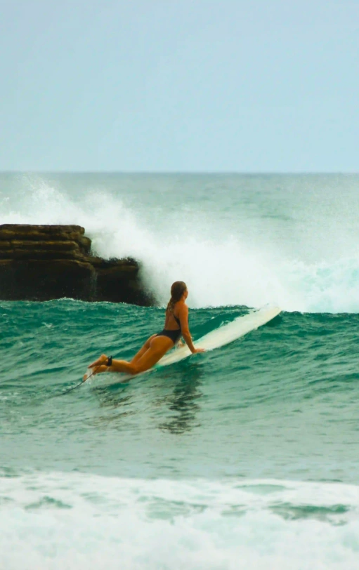 Surfer paddling into a breaking wave near Magnific Rock in Popoyo, Nicaragua, with rocky reef formations