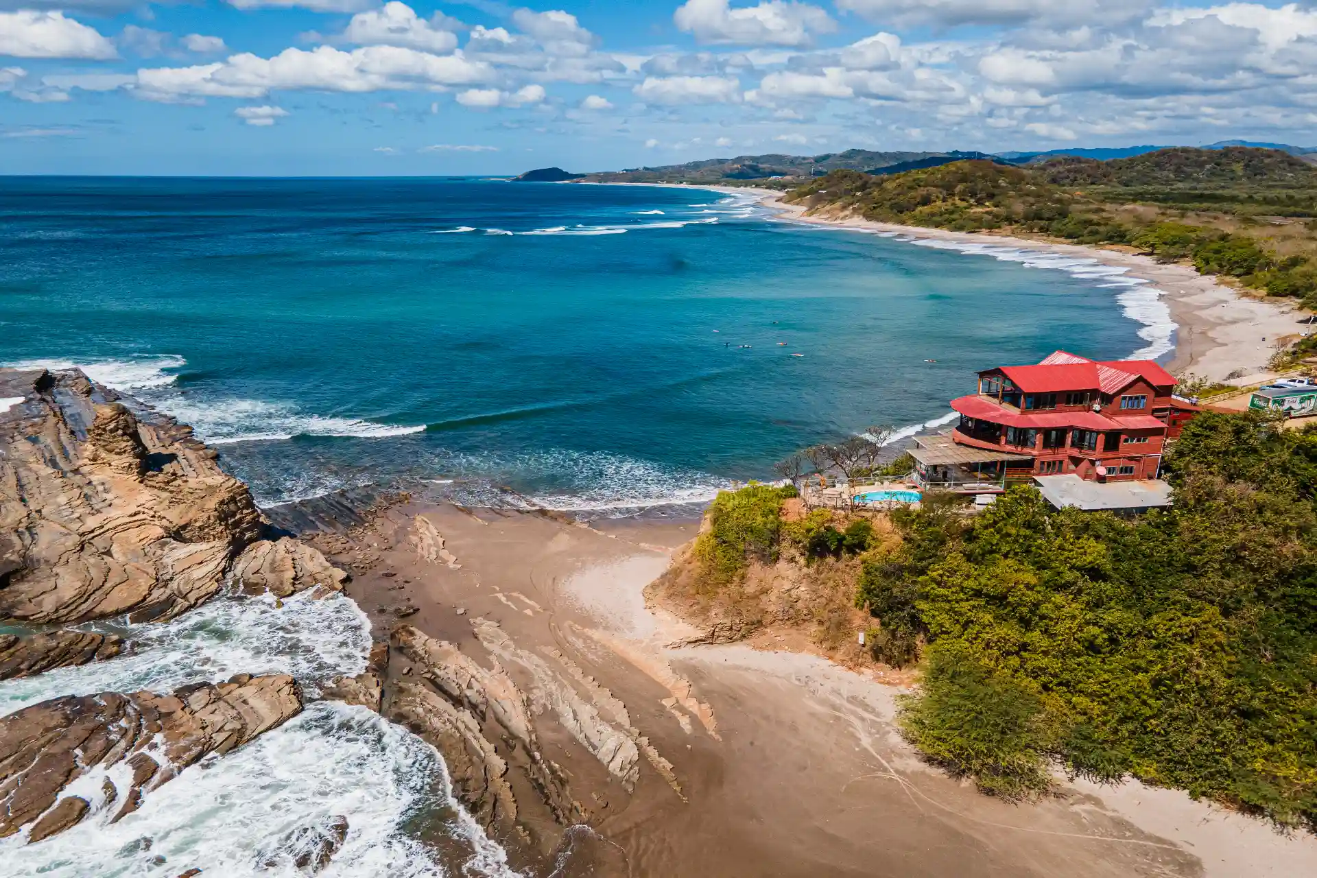 Aerial view of Beginners Bay in Popoyo, Nicaragua, showing the coastline, ocean waves, sandy beach, and magnific rock
