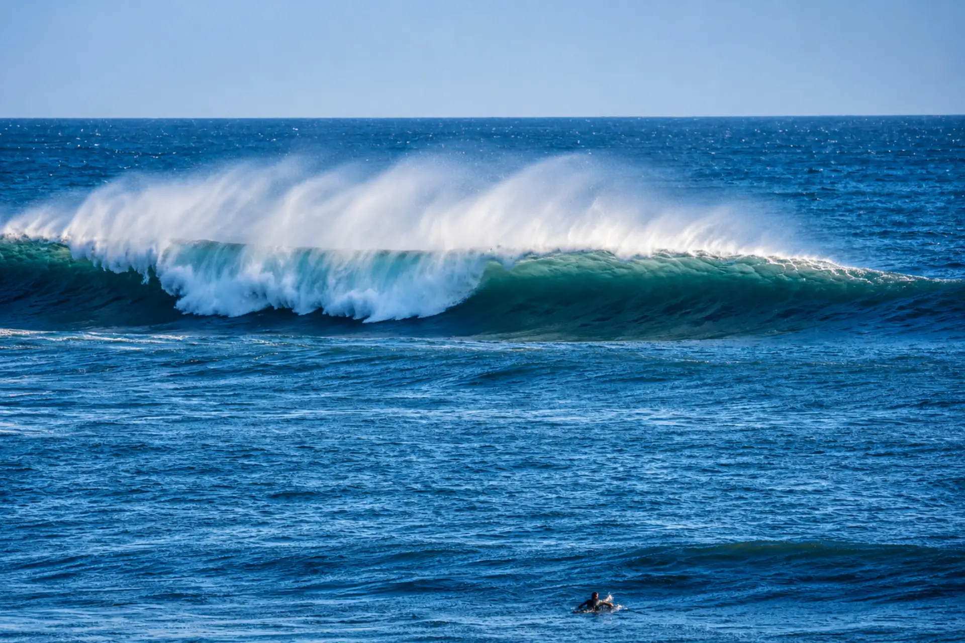 Large ocean wave breaking offshore with a surfer visible in the water